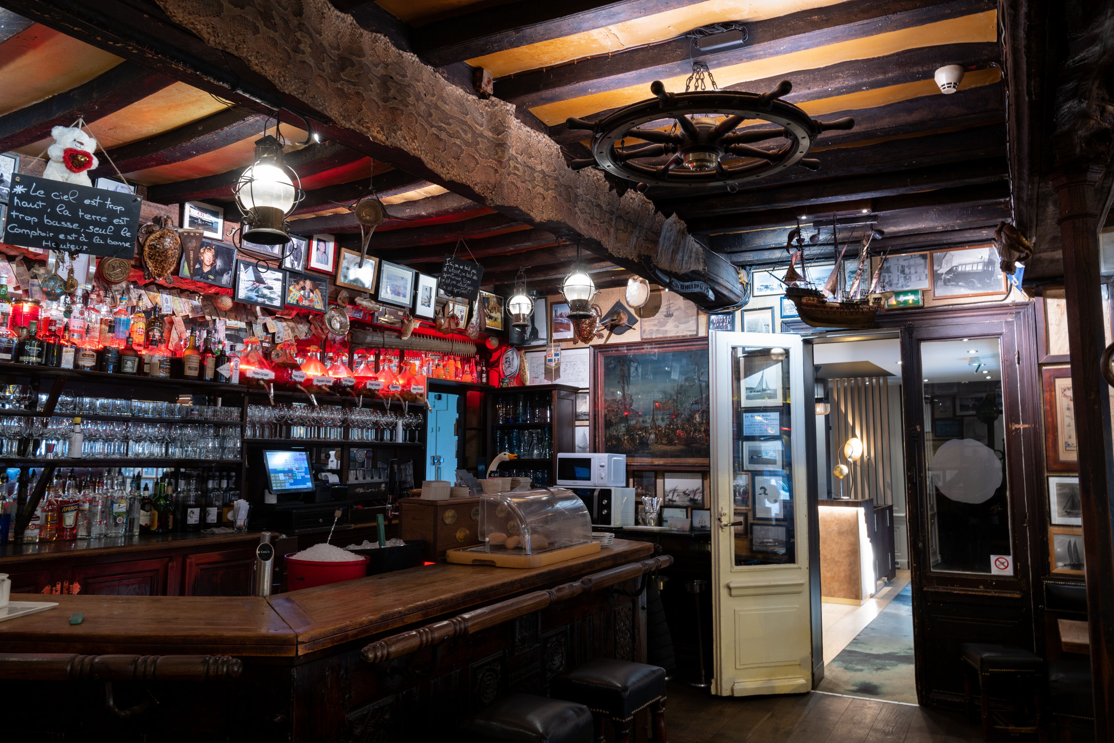 Un bar con vigas de madera, estantes llenos de botellas y una barra con taburetes.