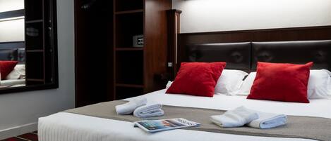 A neatly made bed with red pillows, a magazine, and folded towels.