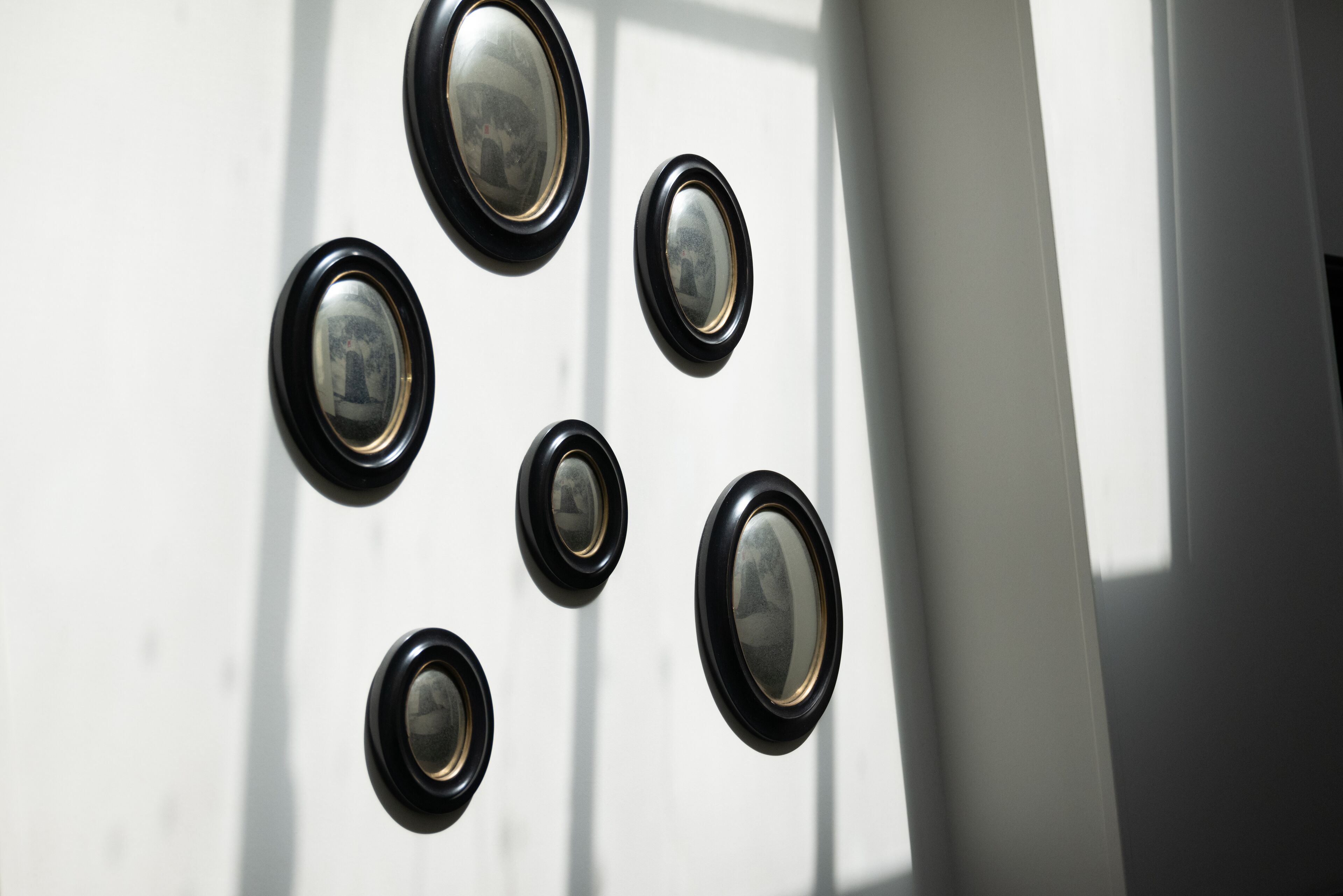 A wall with six framed mirrors of varying sizes.