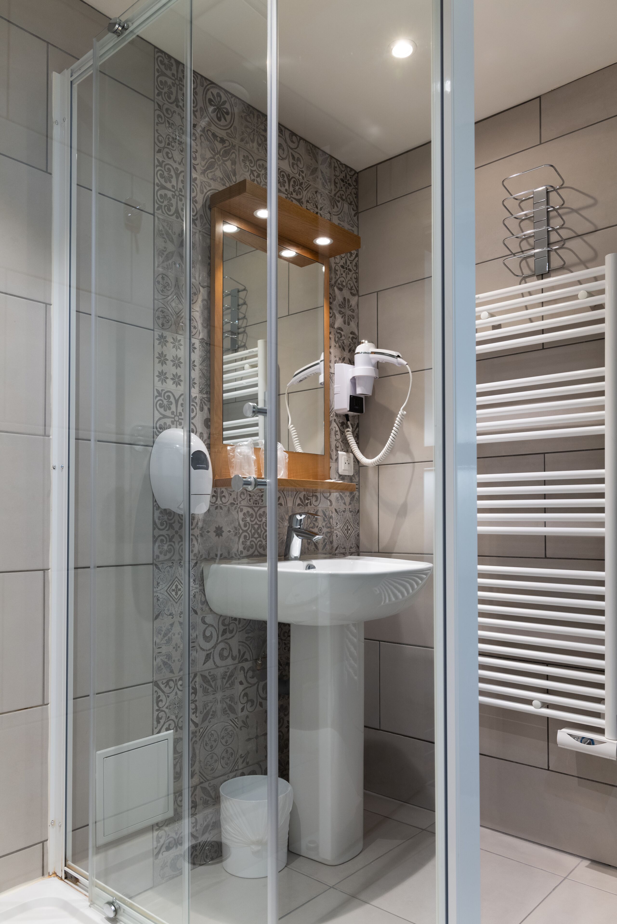 Une salle de bain moderne avec une douche à parois de verre, un lavabo sur colonne, un porte-serviettes et un sèche-cheveux.