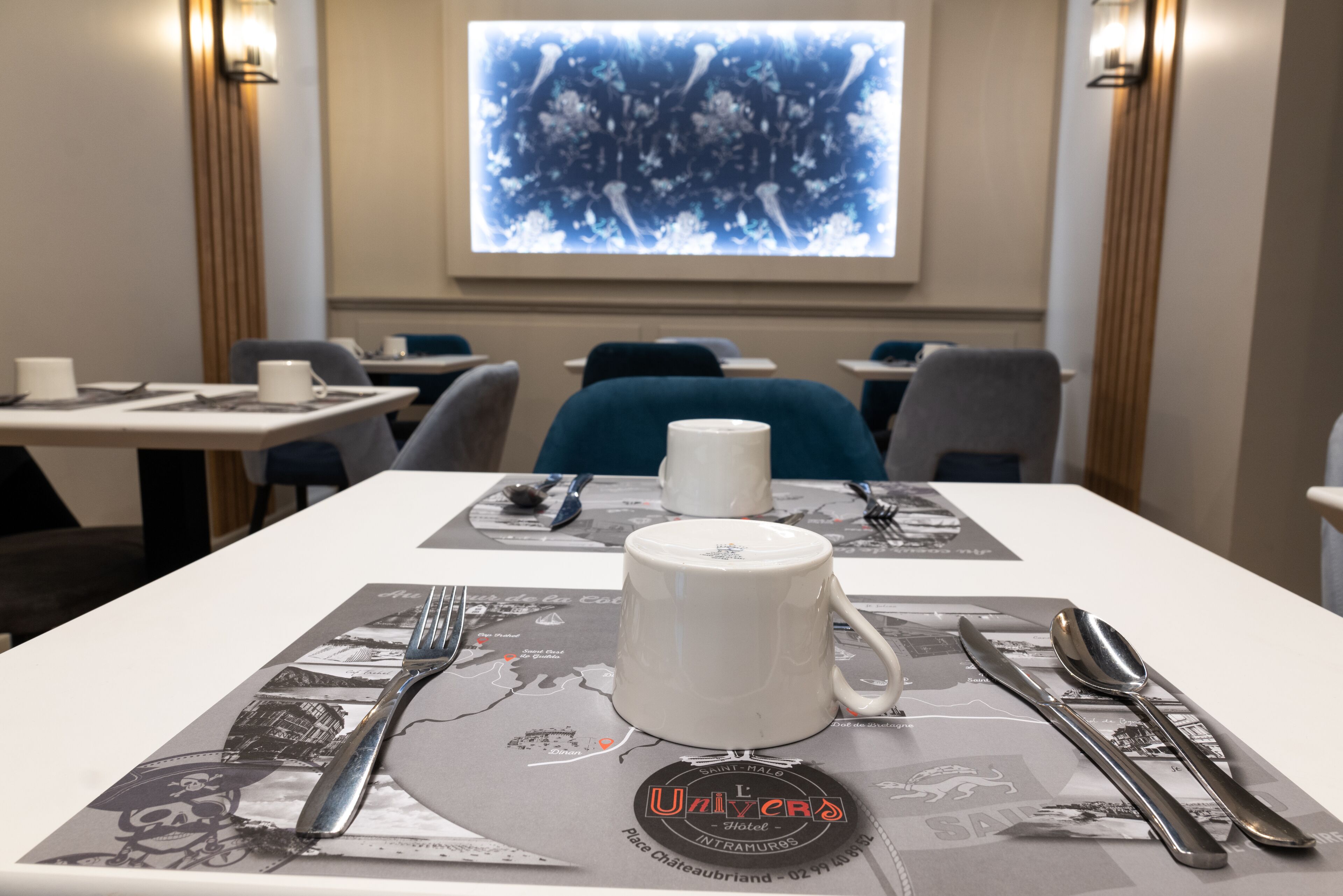 Una mesa de comedor dispuesta con una taza blanca, cubiertos y un mantel individual con un mapa.