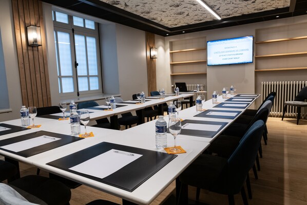 A conference room with long tables, chairs, water bottles, and a screen displaying a welcome message. - Hôtel de l'Univers (Saint-Malo)