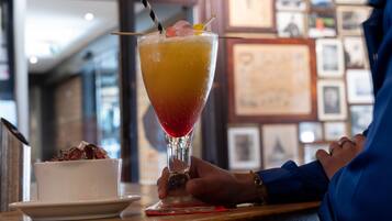 A cocktail in a glass with a straw, garnished with fruit, on a table with a framed picture in the background.