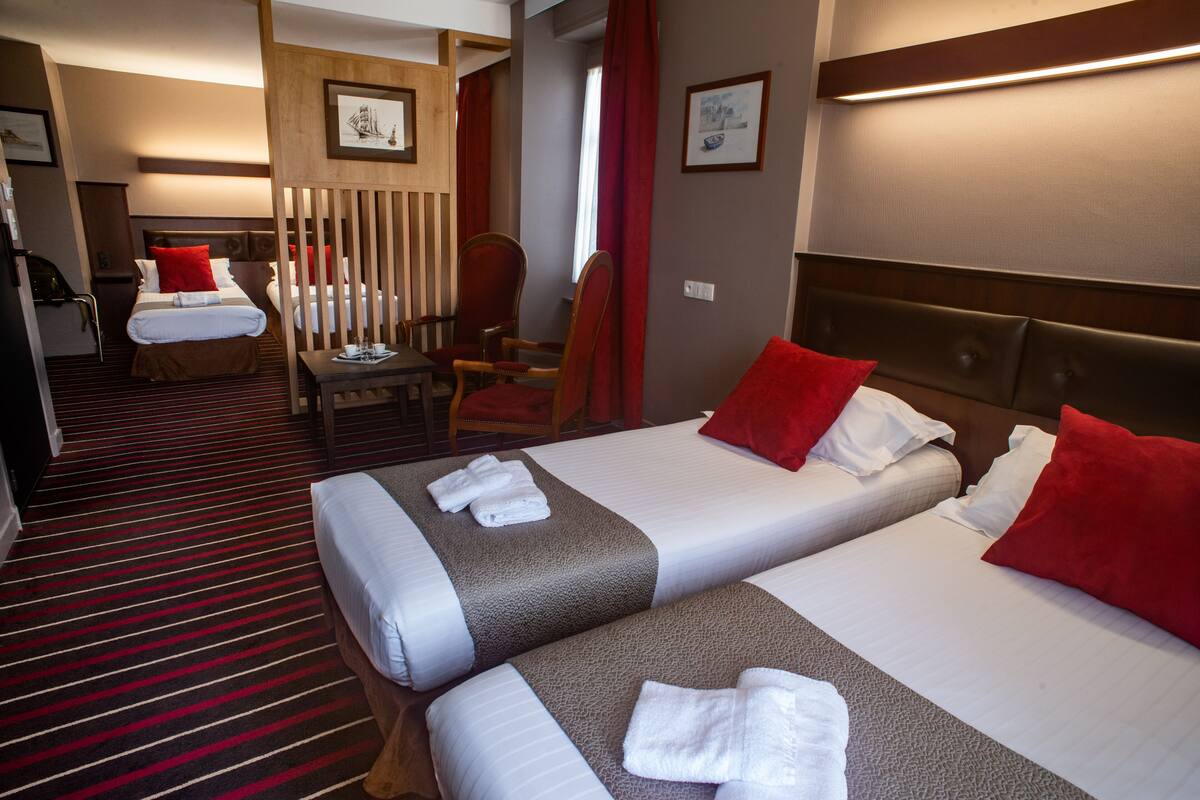 A hotel room with two beds, a wooden headboard, a red and white striped carpet, and a wooden partition.