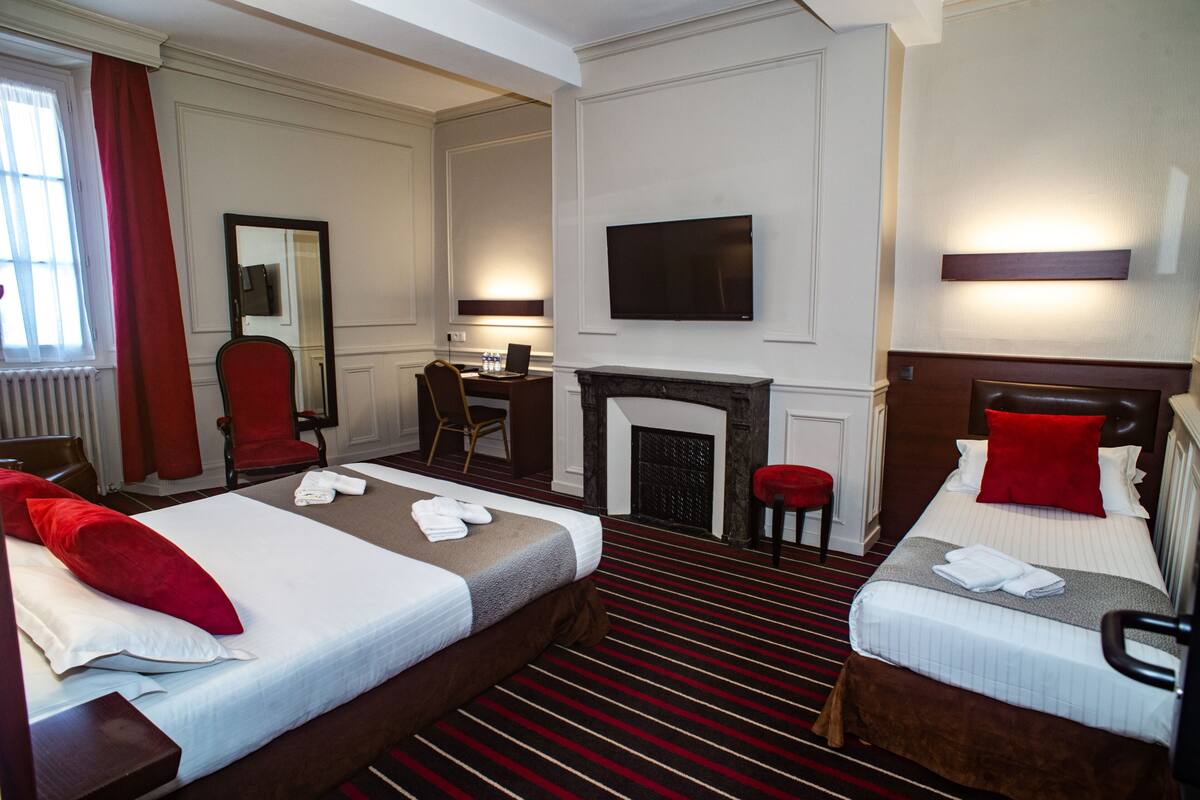 A hotel room with two beds, a fireplace, a desk with a chair, a TV, and a red curtain.