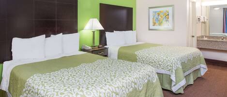 A hotel room with two beds, each with a green bedspread and white pillows. There is a nightstand with a lamp and a phone, and a painting on the wall.