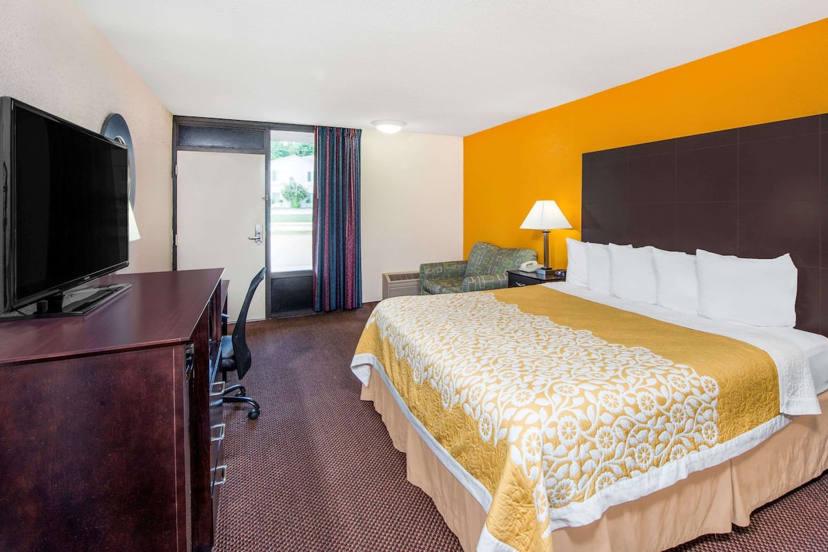 Una habitación de hotel con cama, escritorio con televisor, lámpara y silla.