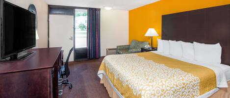 A hotel room with a bed, a desk with a TV, a lamp, and a chair.