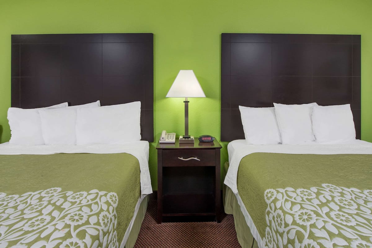 Una habitación de hotel con dos camas, una mesita de noche con lámpara y una pared verde.