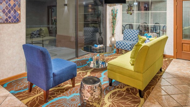 Een woonkamer met een blauwe fauteuil, een gele bank en een glazen salontafel.