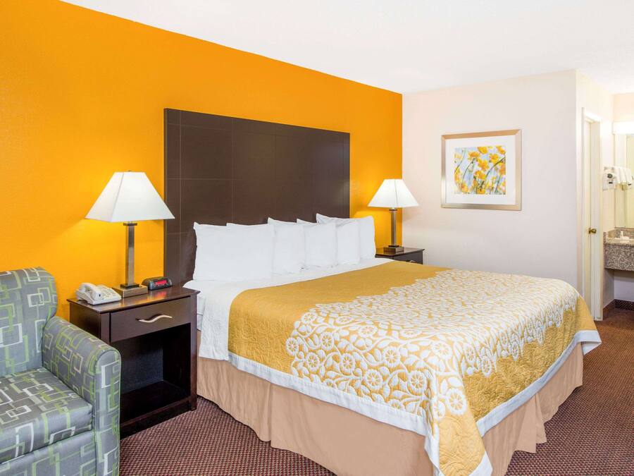 Habitación de hotel con una cama grande, dos mesitas de noche con lámparas, una silla, un escritorio pequeño con teléfono y un cuadro en la pared.
