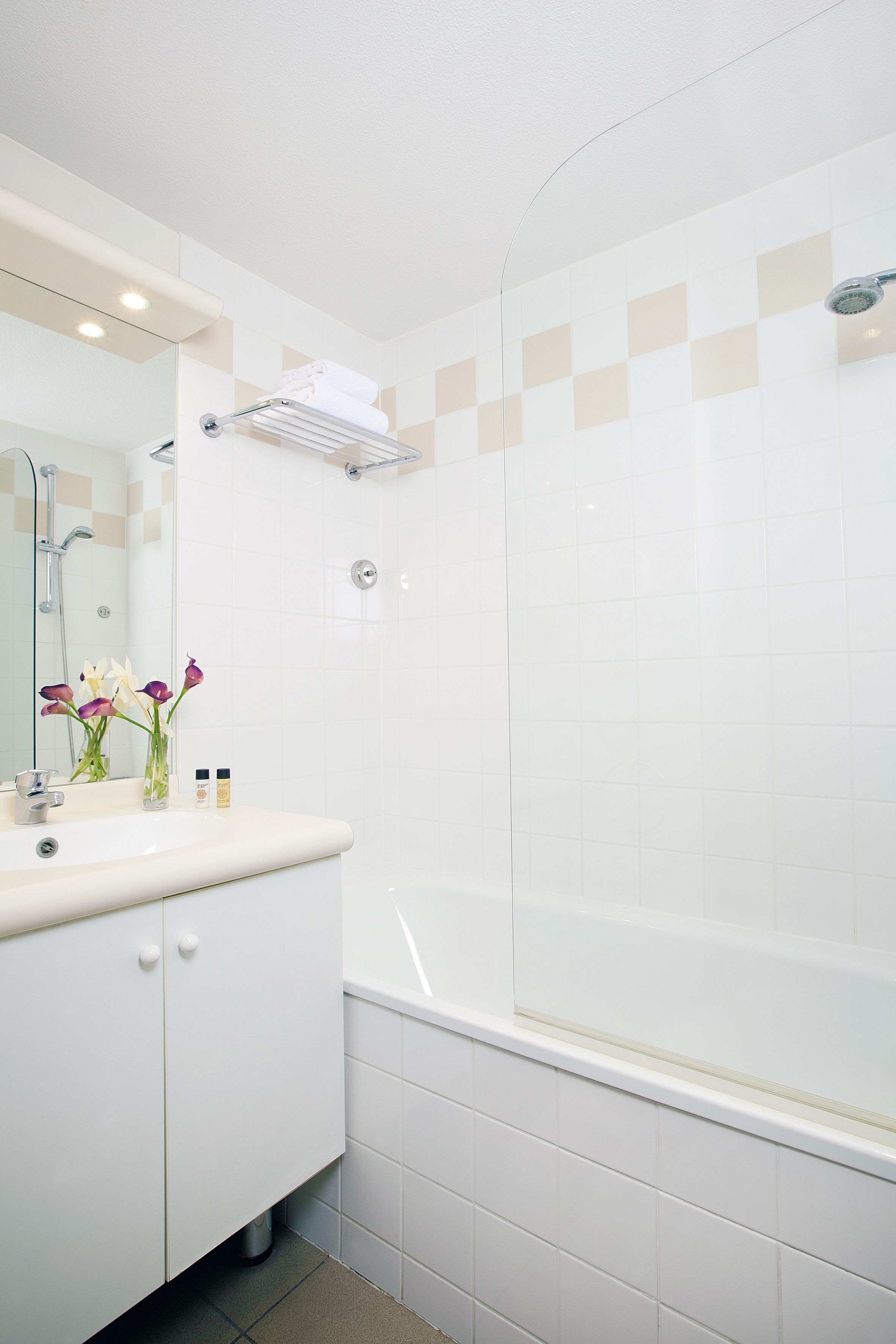 Un baño moderno con tocador blanco, cabina de ducha con vidrio y espejo sobre el lavabo.