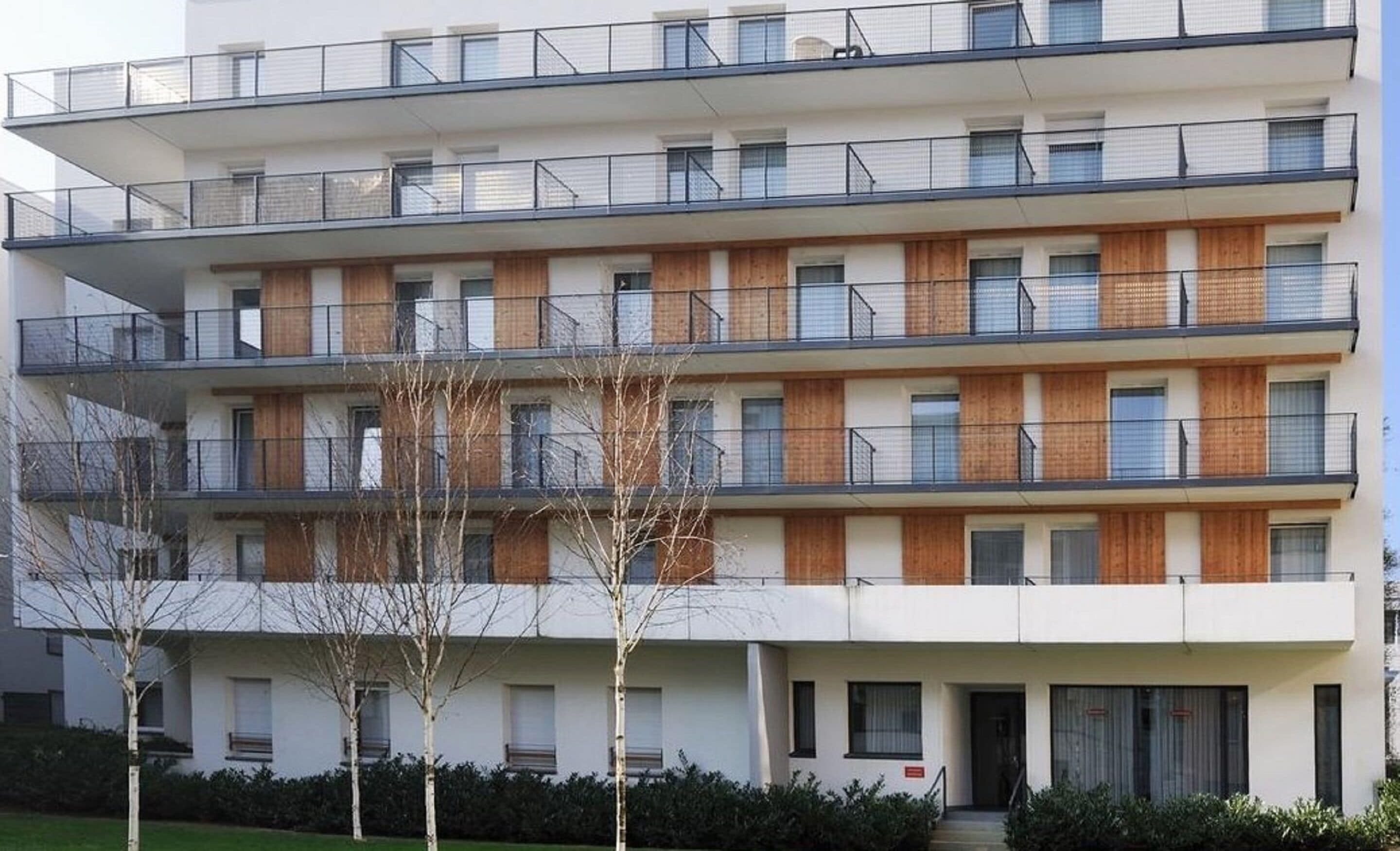 Een meerlaags woongebouw met balkons, houten lambrisering en een plat dak.