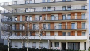 A multi-story residential building with balconies, wooden paneling, and a flat roof.