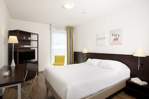 Ein Hotelzimmer mit einem Bett, einem Schreibtisch mit Lampe, einem Fernseher, einem Sessel und einem Nachttisch mit Lampe.