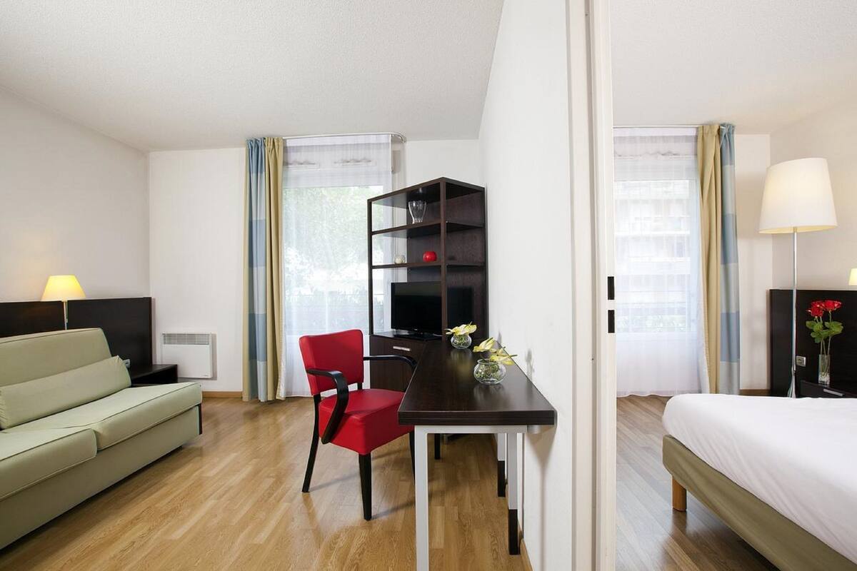 Een hotelkamer met een bed, een bureau met een computer, een rode stoel, een bank en een televisie.