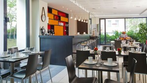 A modern dining area with multiple tables and chairs, a counter with a variety of items, and large windows offering a view of greenery outside. - Residhome Appart Hotel Nancy Lorraine (Nancy)
