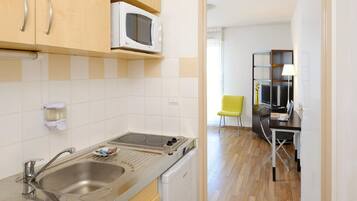 A compact kitchen with a microwave, sink, and dishwasher. A dining area with a table and chairs is visible in the background.
