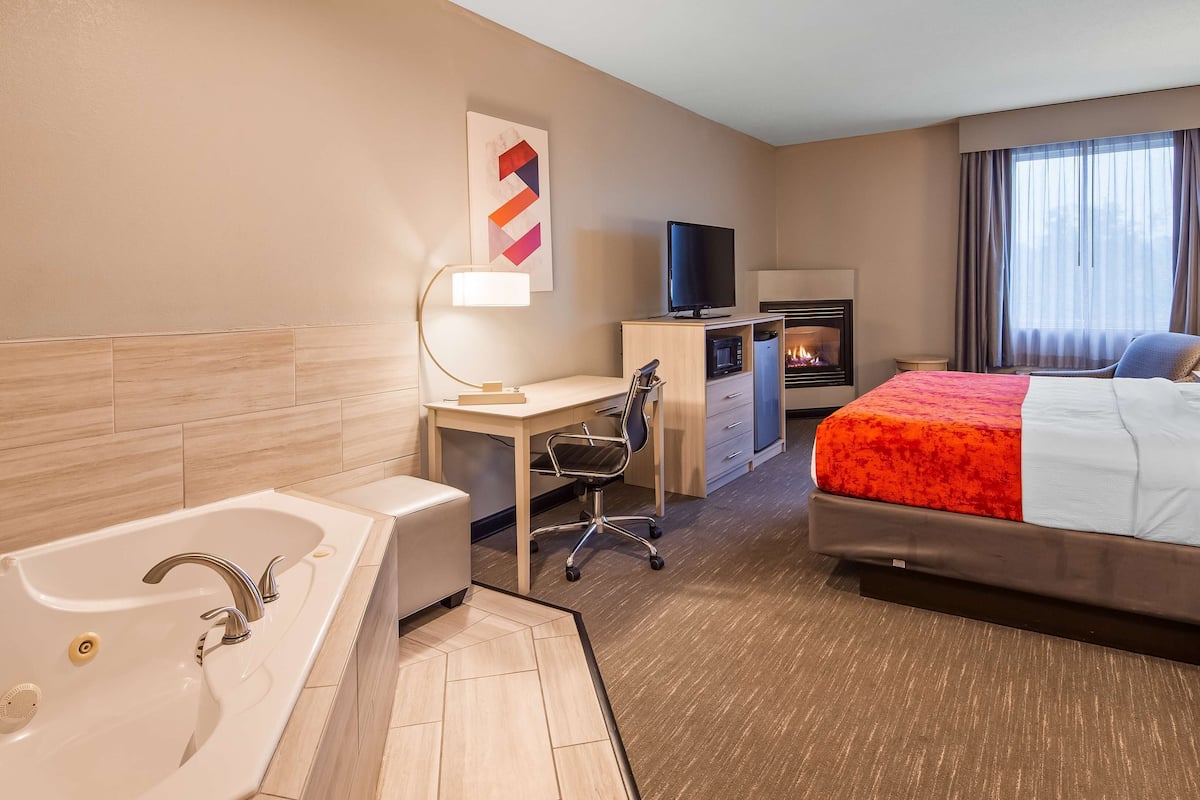 Een hotelkamer met een groot bed, een bureau met computer, een televisie, een openhaard en een badkamer met badkuip en wastafel.