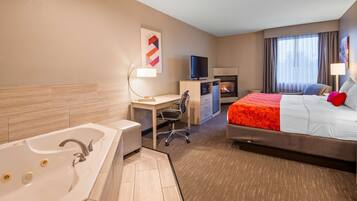 Habitación de hotel con una cama grande, un escritorio con computadora, televisor, chimenea y baño con bañera y lavamanos.