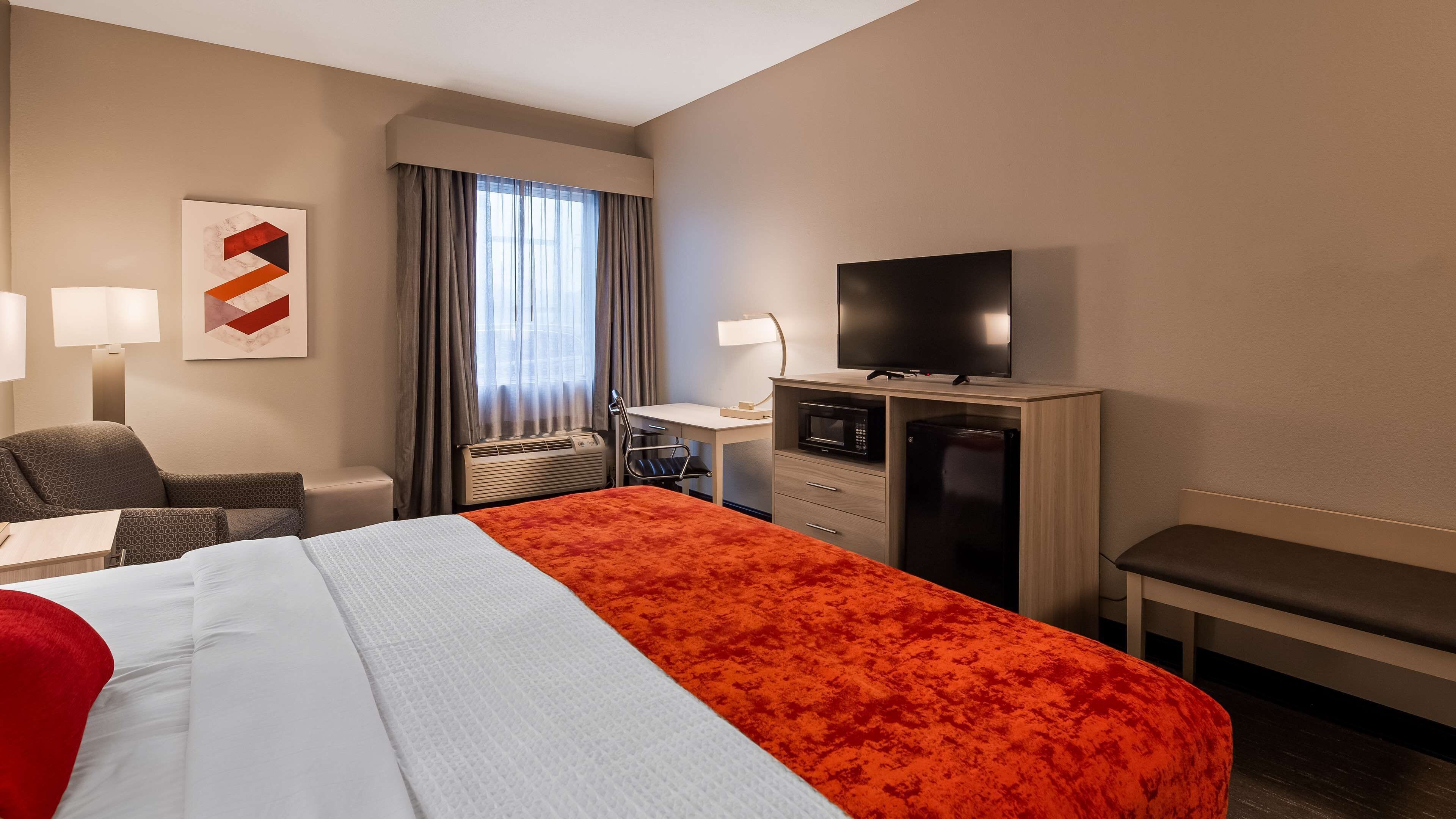 A hotel room with a bed, a desk, a television, a microwave, and a refrigerator.