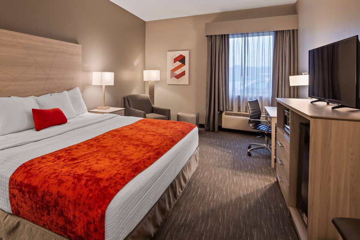 Een hotelkamer met een groot bed, een bureau, een stoel, een televisie en een raam met gordijnen.
