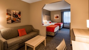 Habitación de hotel con sofá, una mesita, dos camas con ropa de cama roja y blanca, un cuadro en la pared y una ventana con cortinas.