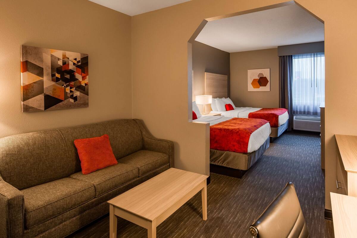 Hotelkamer met een bank, een kleine tafel, twee bedden met rode en witte beddengoed, een schilderij aan de muur en een raam met gordijnen.