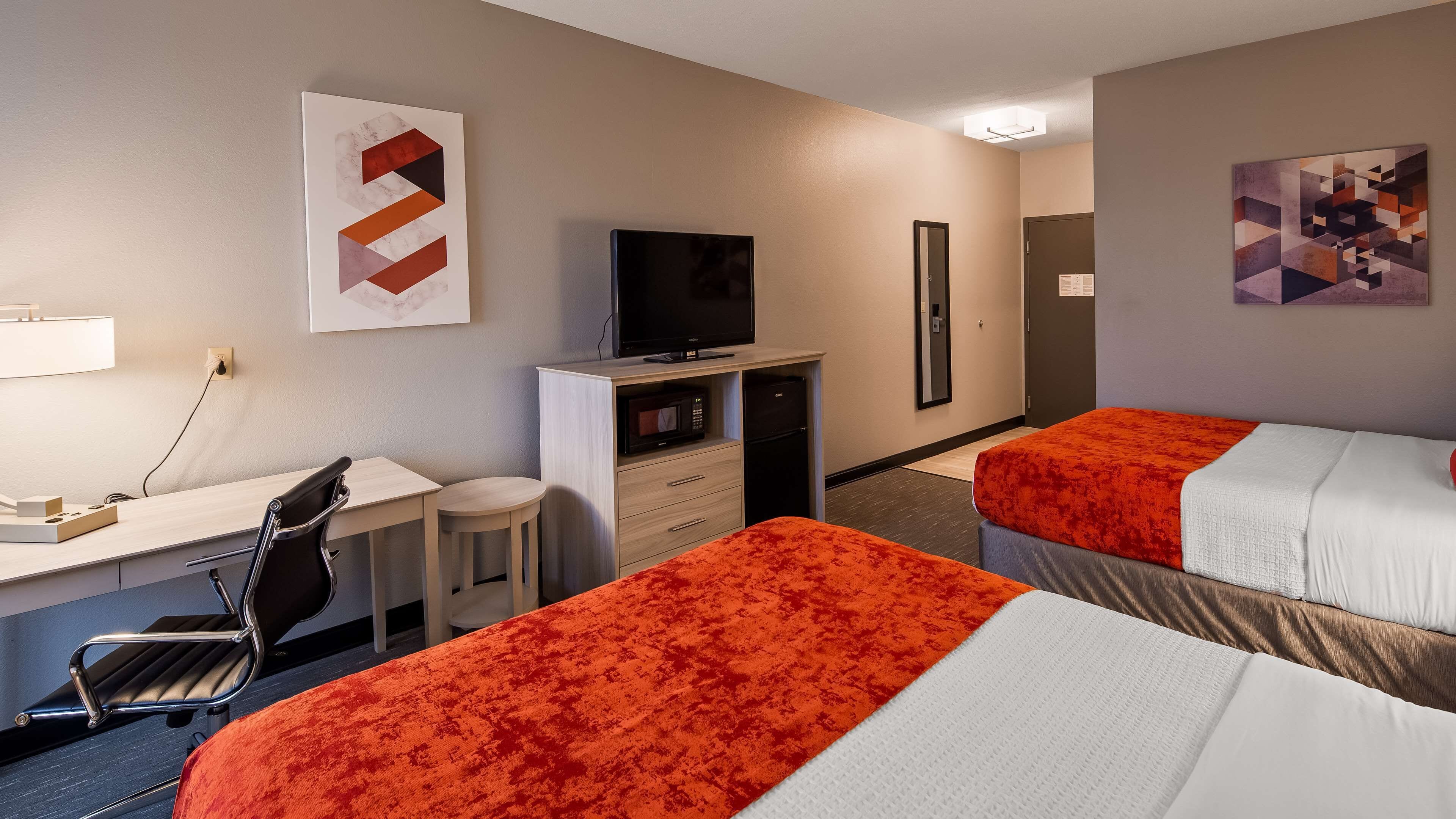 Quarto de hotel com duas camas, uma mesa, uma cadeira, uma TV, micro-ondas e frigorífico.