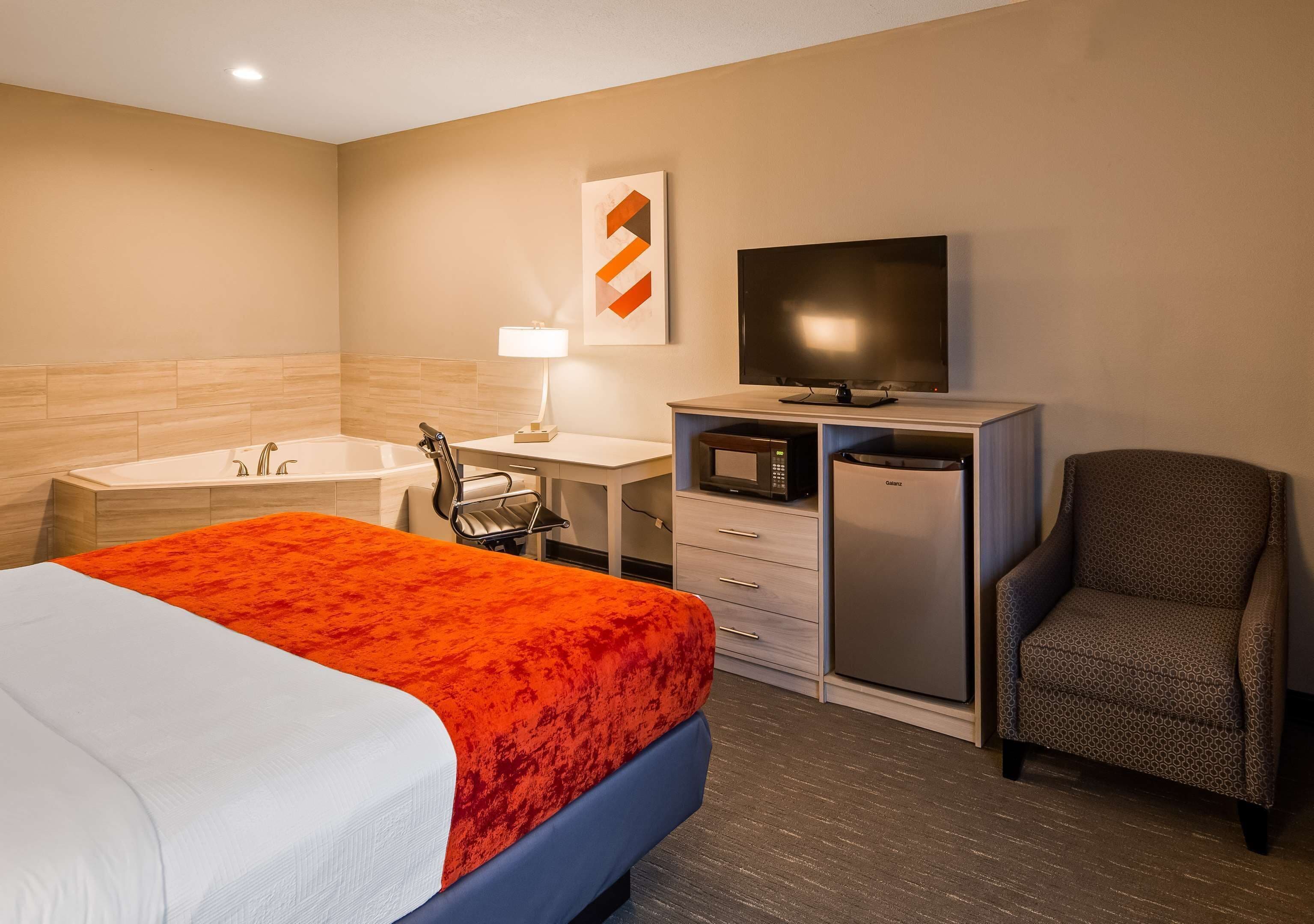 A hotel room with a bed, a desk, a television, a chair, a microwave, and a refrigerator.
