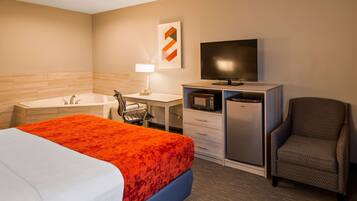 A hotel room with a bed, a desk, a television, a chair, a microwave, and a refrigerator.