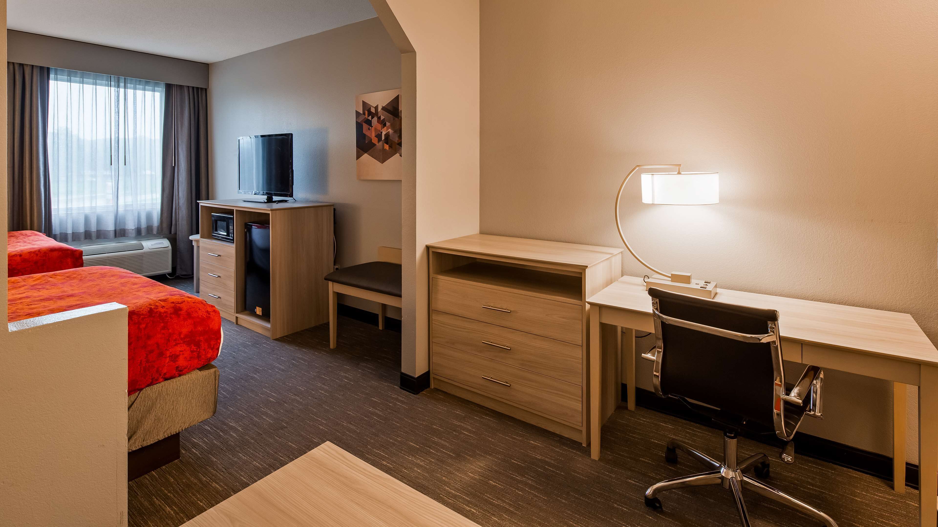 Une chambre d’hôtel avec un lit, un bureau, une chaise, une télévision et une lampe.
