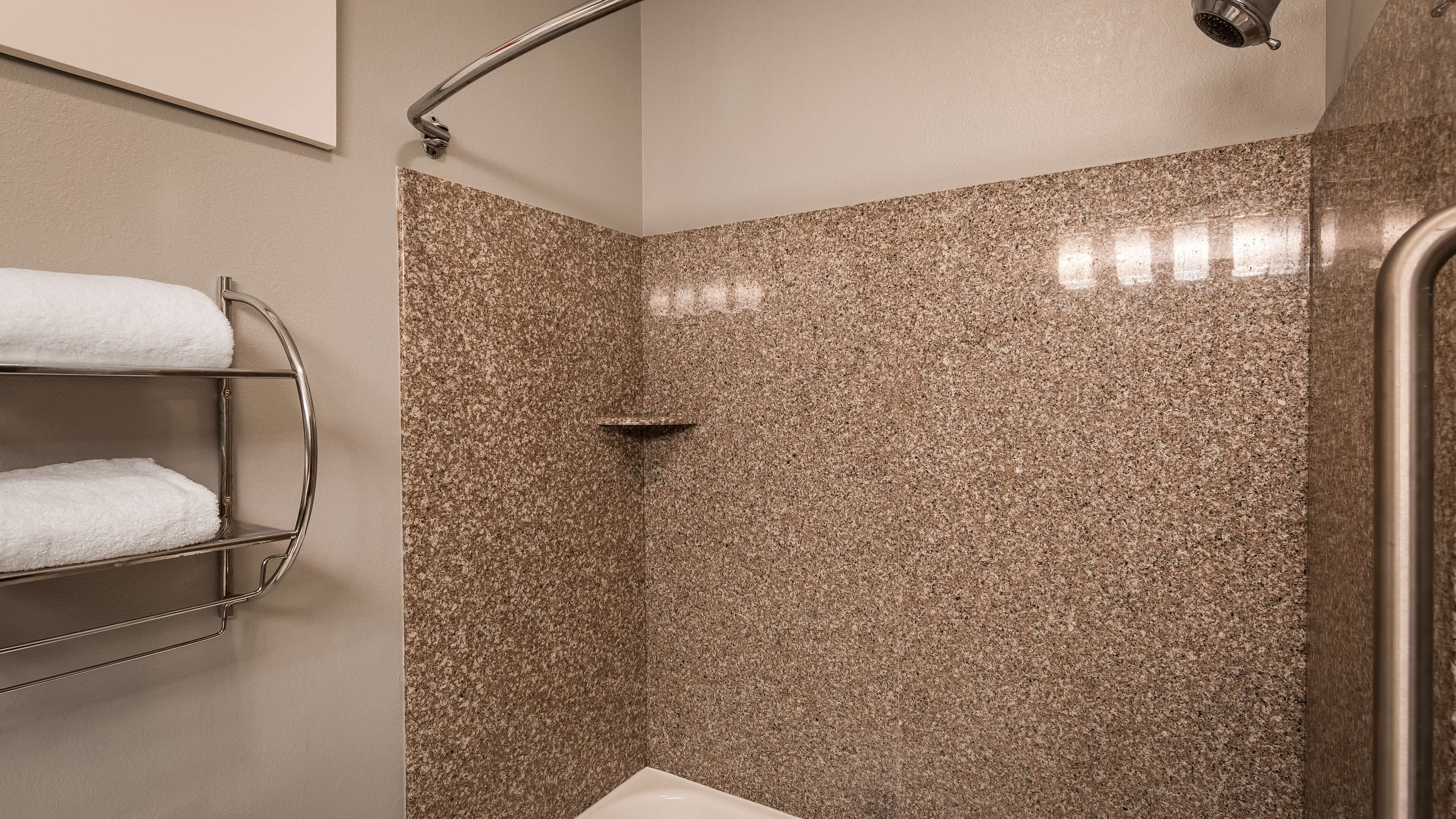 Un baño con ducha, un perchero con dos toallas blancas y una pared revestida de granito.