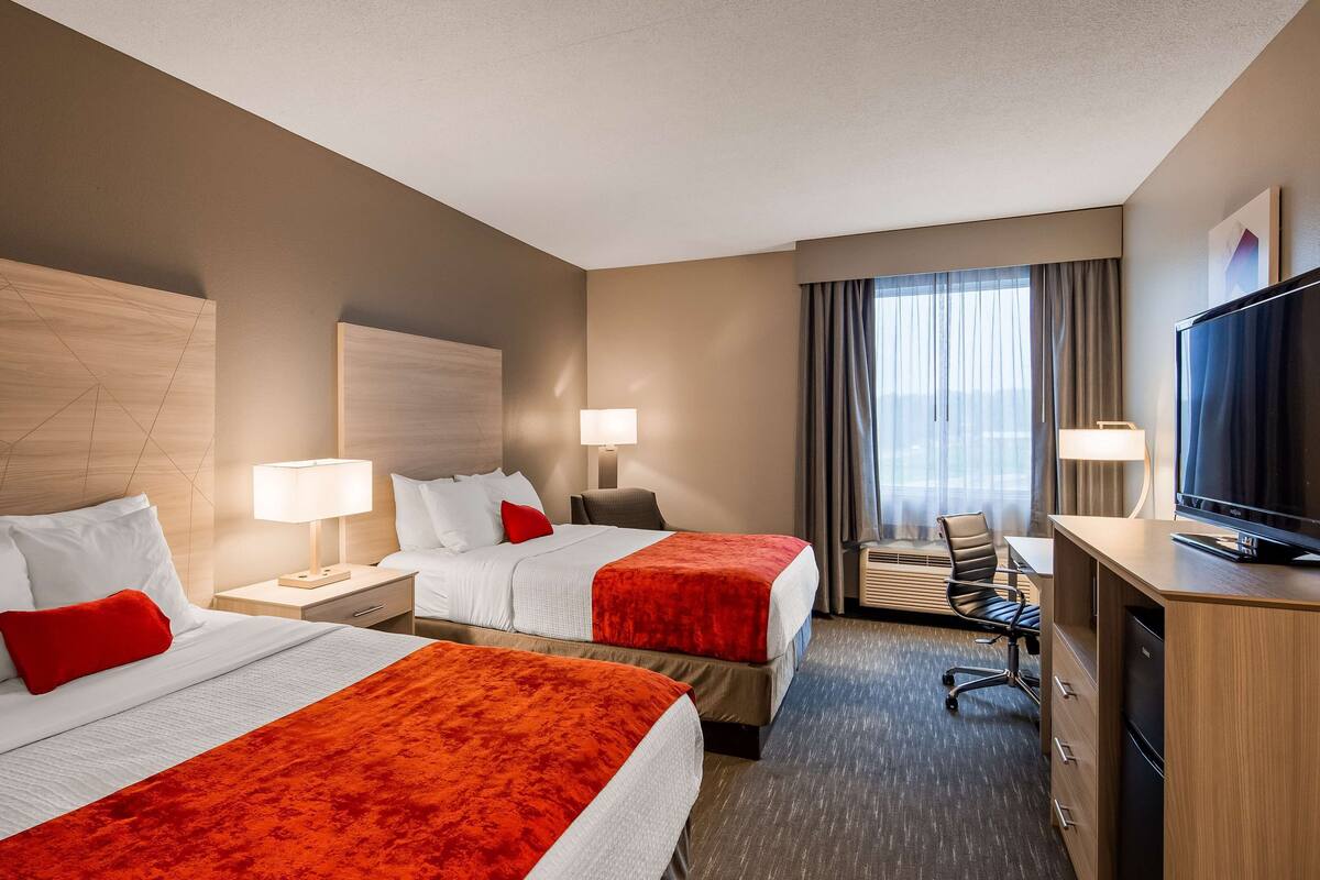 Een hotelkamer met twee bedden, een bureau, een televisie en een raam met gordijnen.