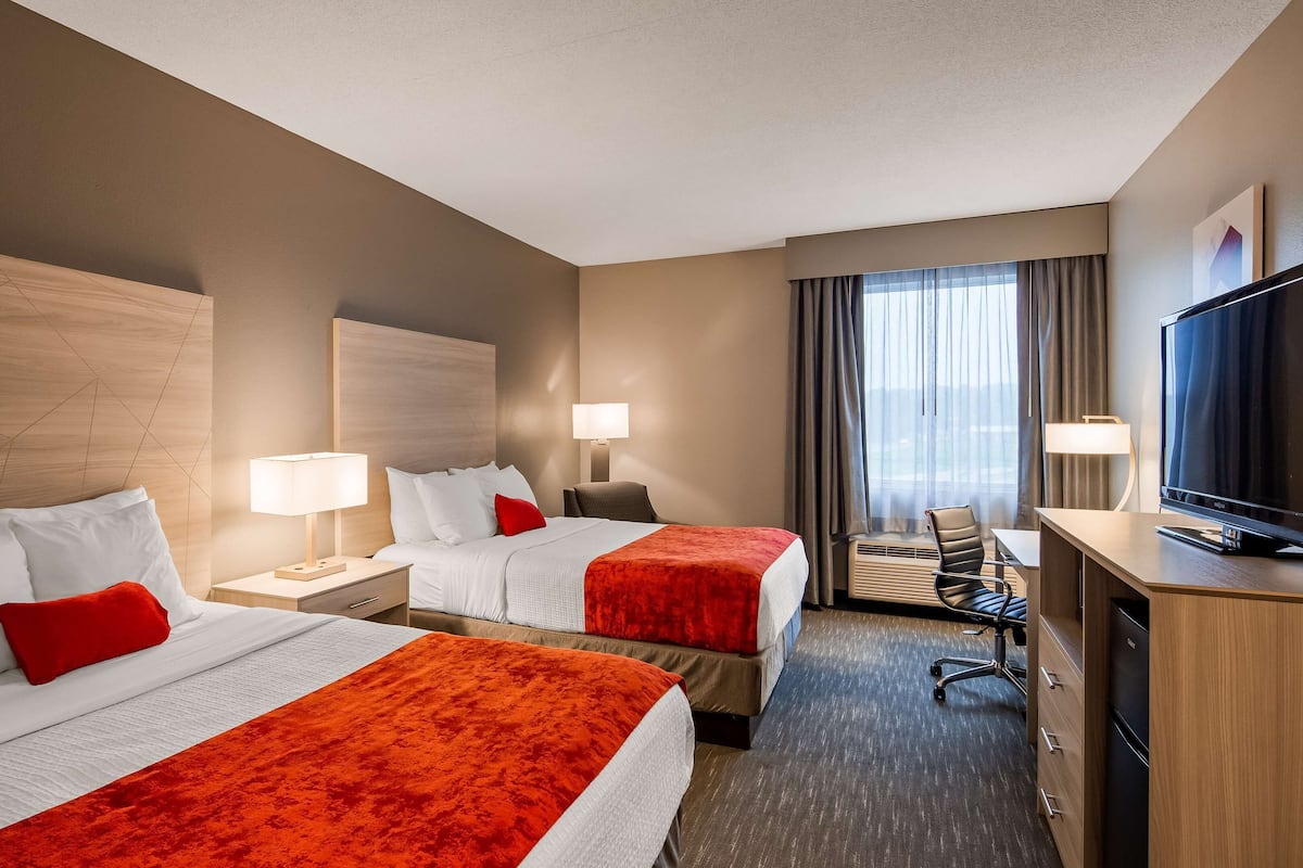 A hotel room with two beds, a desk, a television, and a window with curtains.