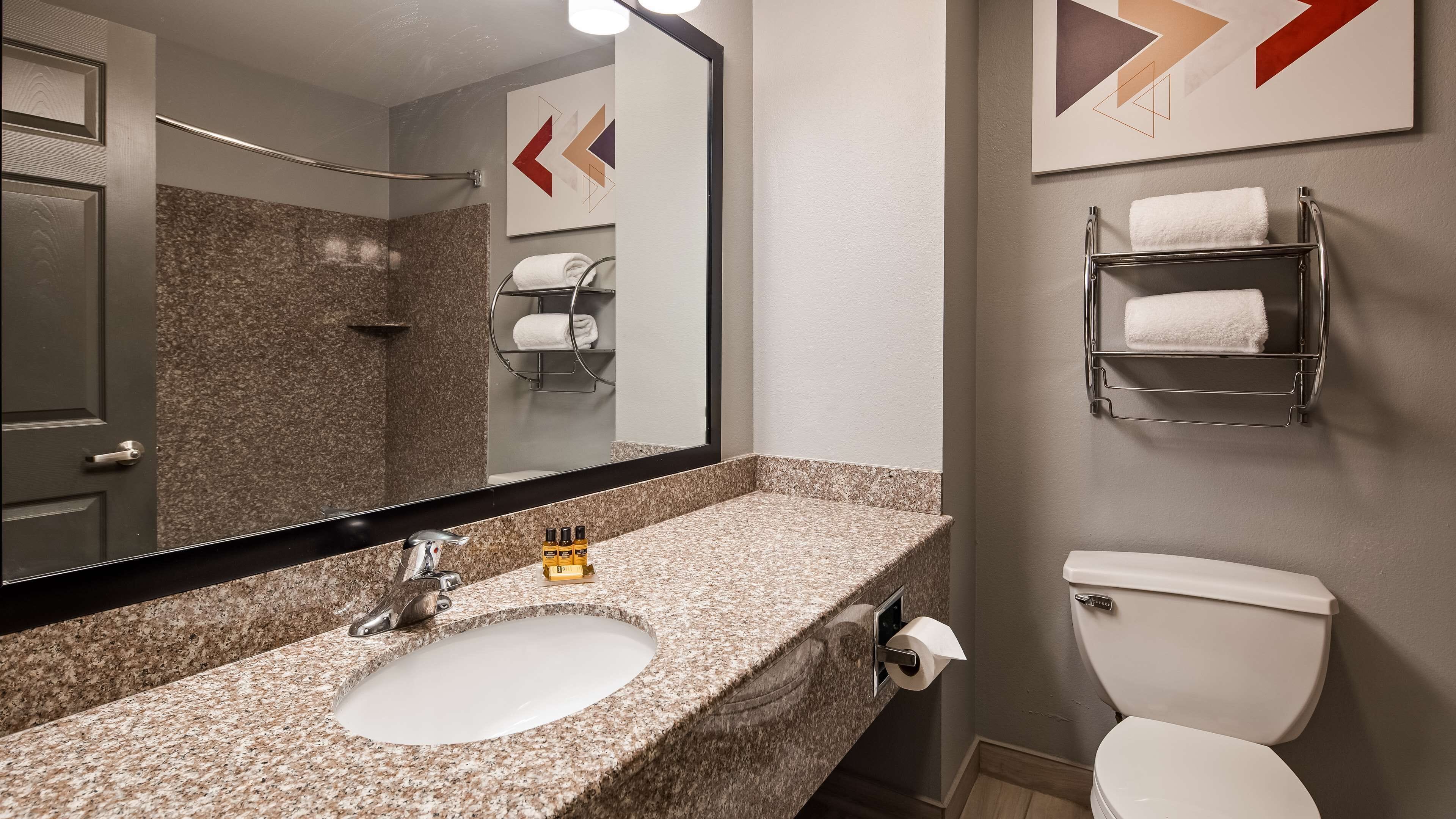 A bathroom with a granite countertop sink, a mirror, a toilet, and a towel rack.