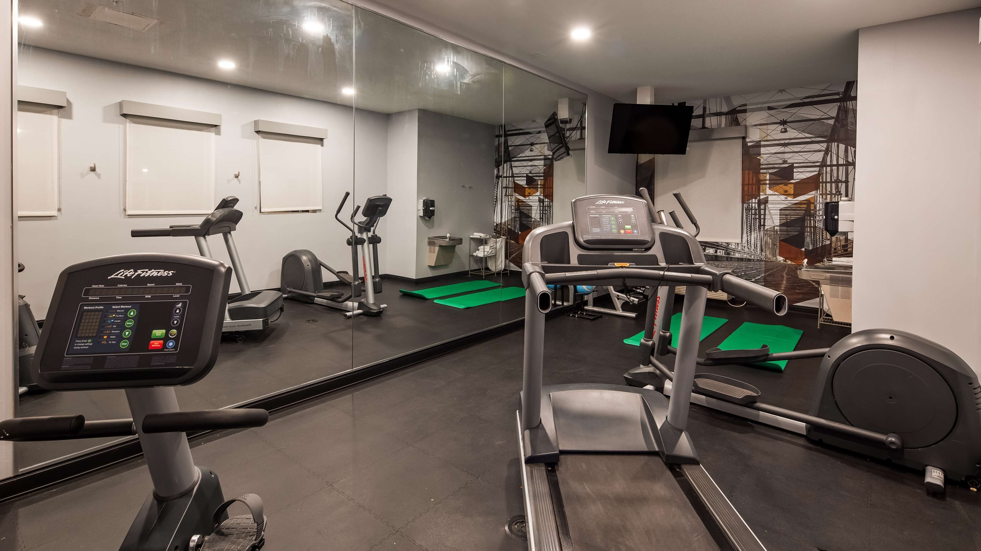 A gym with cardio machines, a mirrored wall, and a television on the wall.