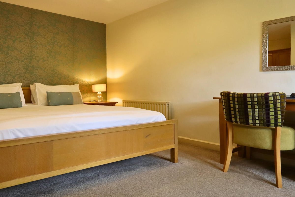 Un dormitorio con una cama de madera, dos mesitas de noche con lámparas, una silla y un espejo en la pared.