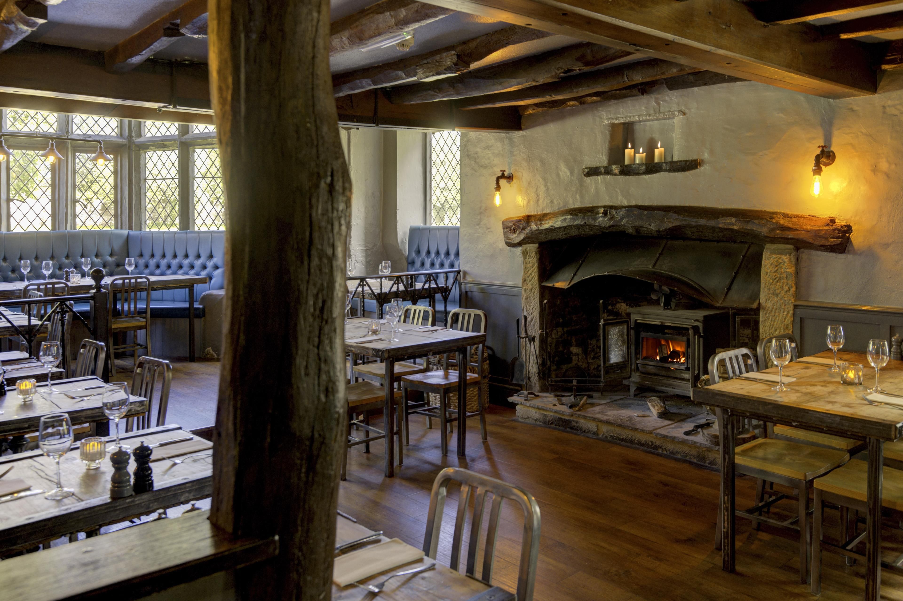 Een restaurant met houten tafels en stoelen, een stenen open haard en uitzicht door een raam met een grillwerkontwerp.