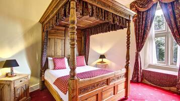 A four-poster bed with a wooden frame and a canopy, a bedside table with a lamp, and a window with curtains.