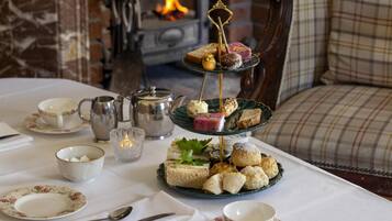 A three-tiered dessert stand with various pastries on a table, surrounded by tea cups, a teapot, and a candle.