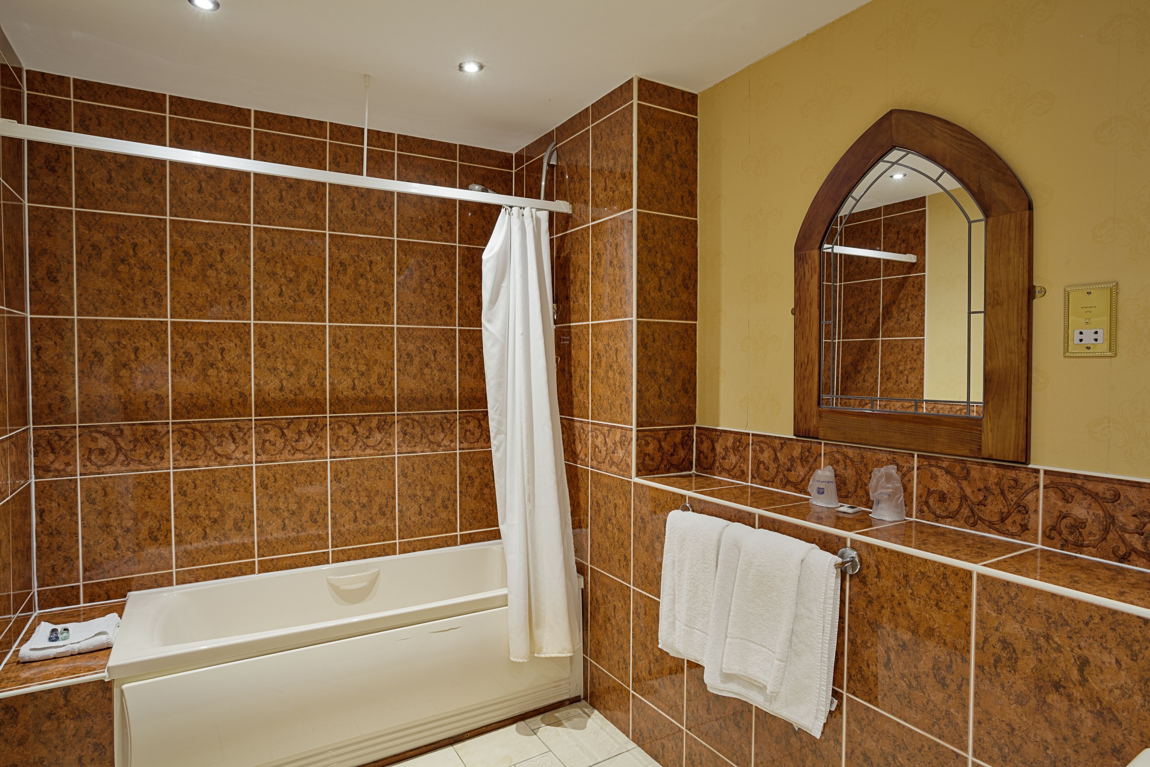 A bathroom with a bathtub, a shower curtain, a towel rack with towels, and a mirror with an arched frame.