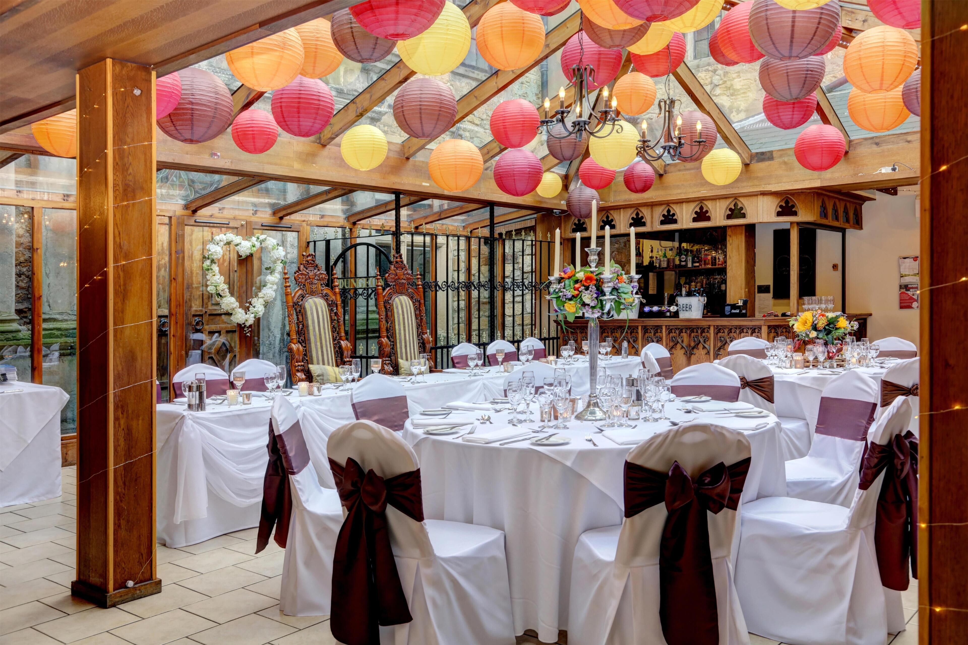 Een feestzaal met ronde tafels, witte tafelkleden en stoelen versierd met linten.