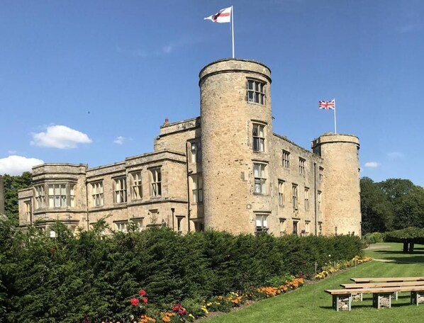 A historic stone building with a central tower and flag, surrounded by well-maintained gardens and a picnic area.
