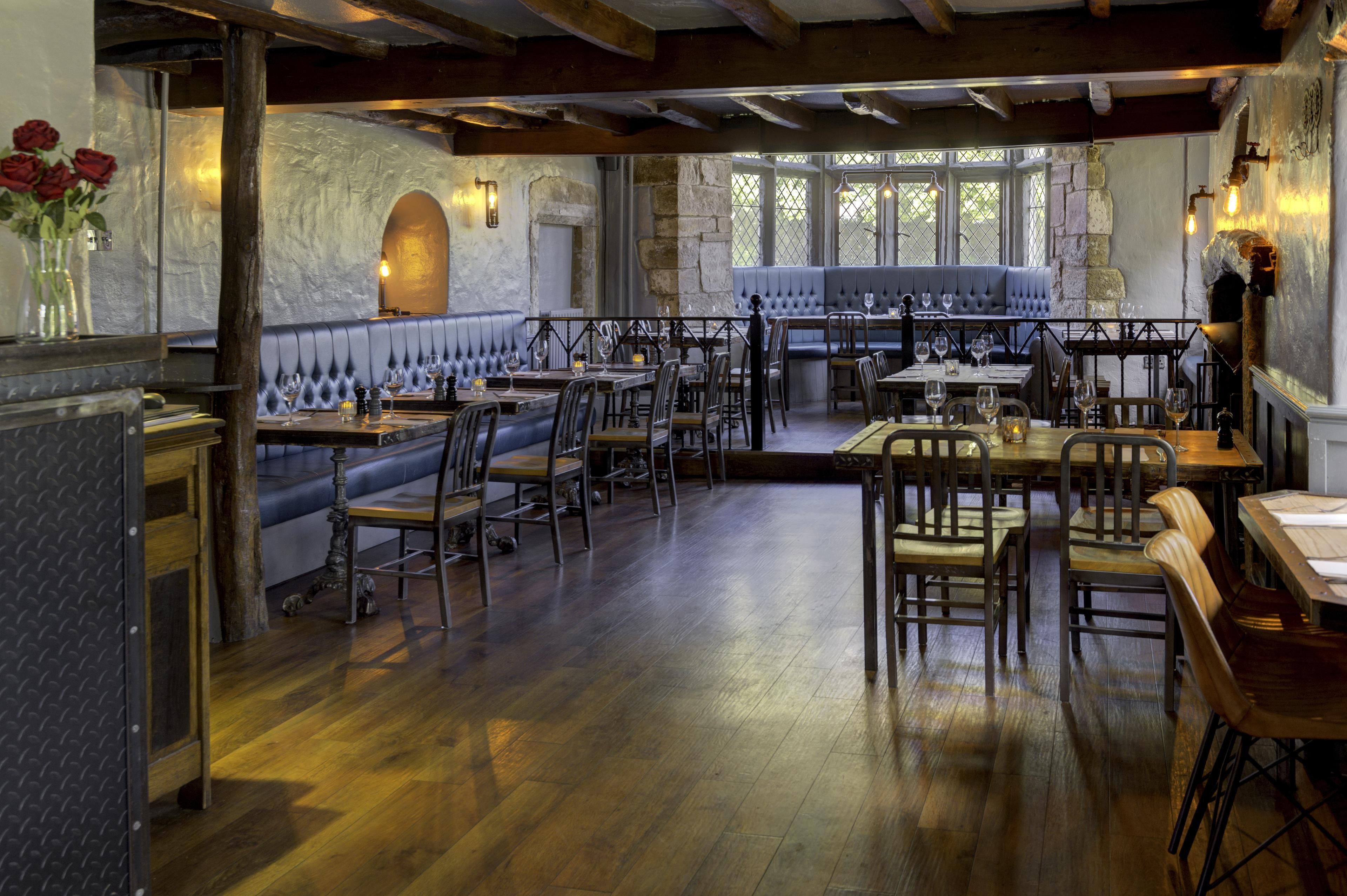 A restaurant with wooden floors, leather booths, and a stone wall.