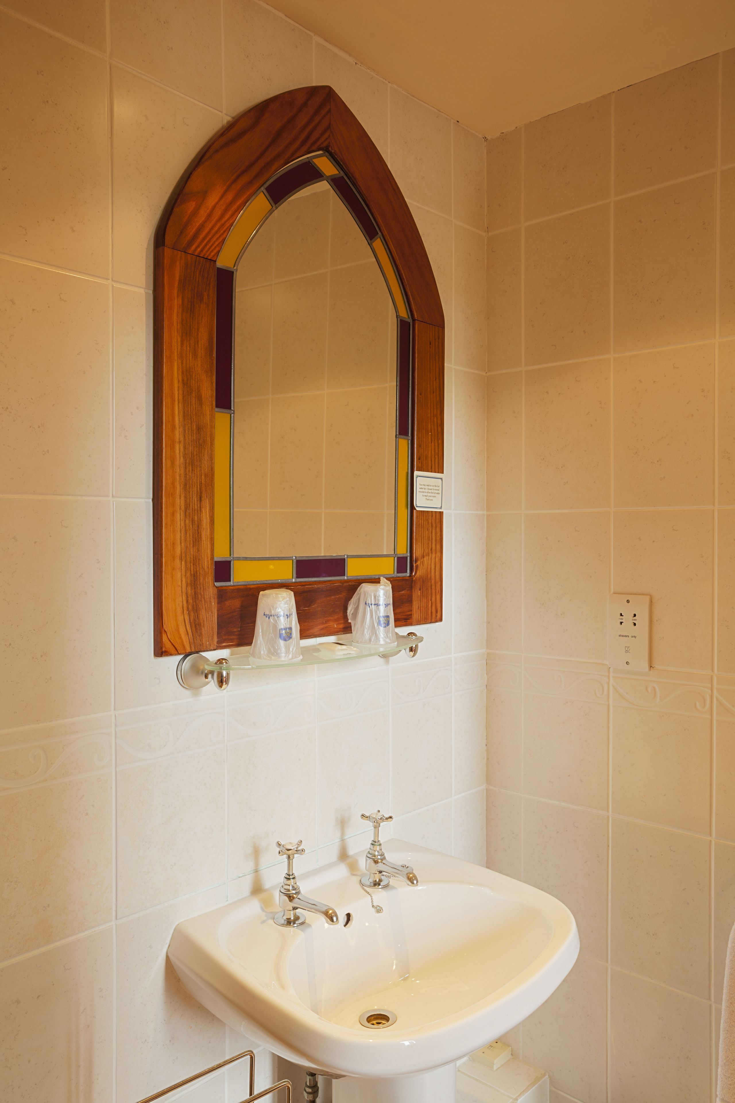 Ein Badezimmer mit einem weißen Waschbecken, einem spiegel mit Holzrahmen und einer gefliesten Wand.