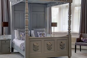 Ein Bett mit Baldachin, grau gestrichen und mit dekorativen Blattfriesen, steht in einem Zimmer mit großem Fenster und grauer Wand.