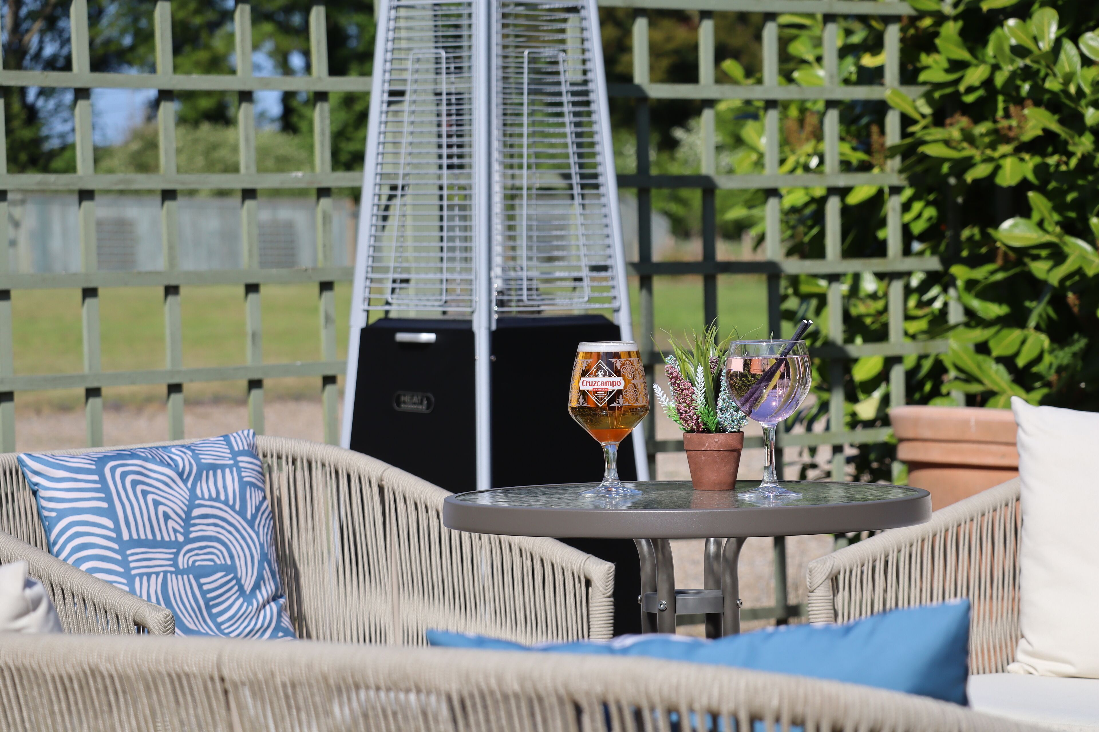 A wicker chair with a blue pillow, a small round table with a glass of beer and a potted plant.