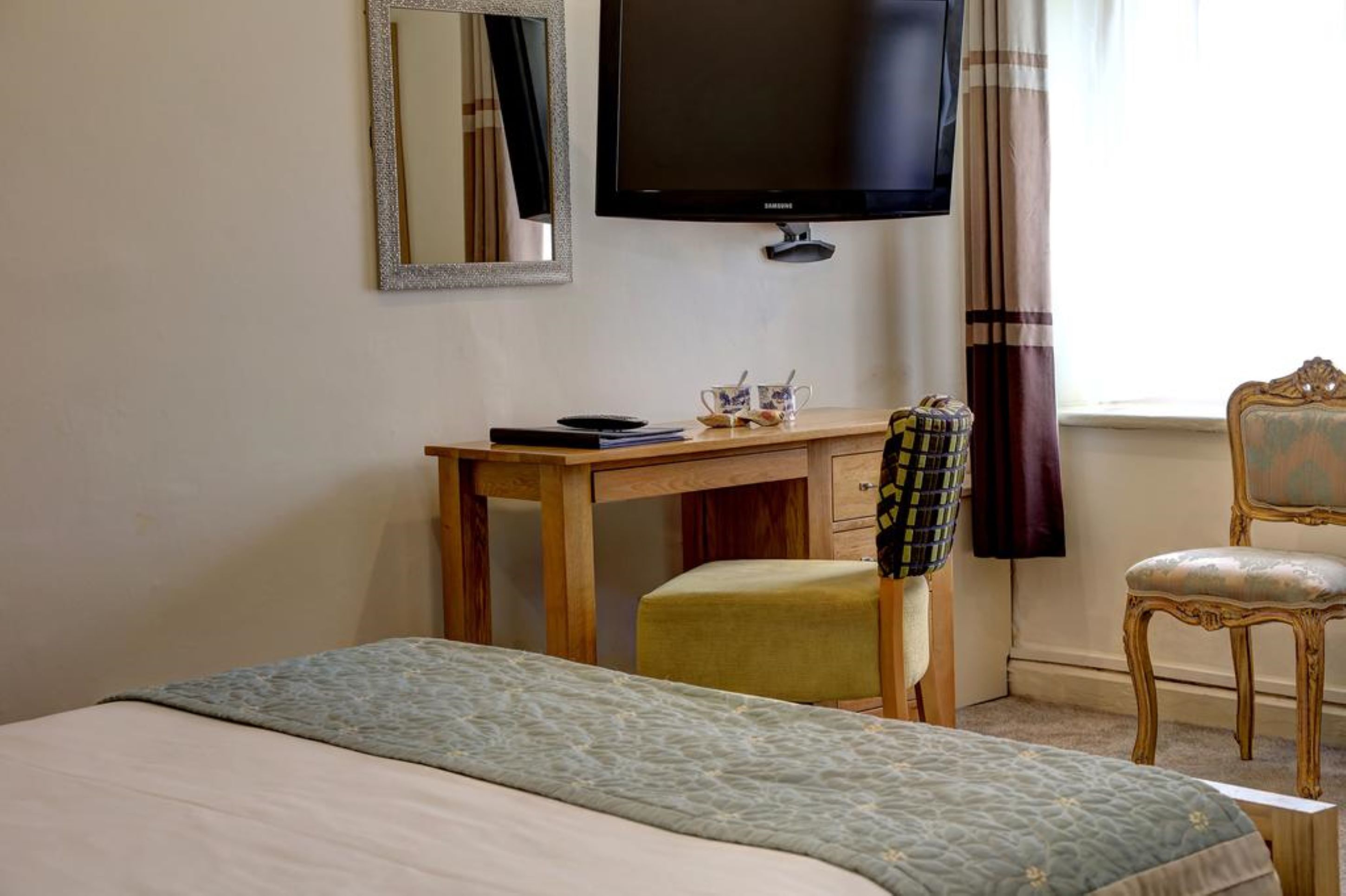 A bedroom with a bed, a desk with a chair, a television, and a window with curtains.
