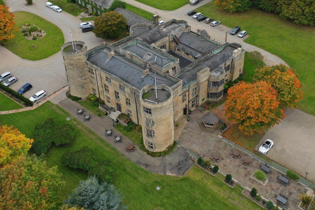 A large, historic building with a central tower, multiple wings, and a courtyard with outdoor seating.